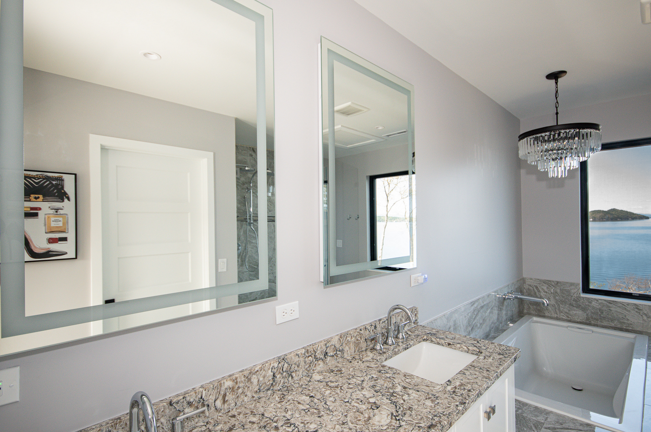 Luxurious space with a granite bathroom countertop, mirrors, and a bathtub.