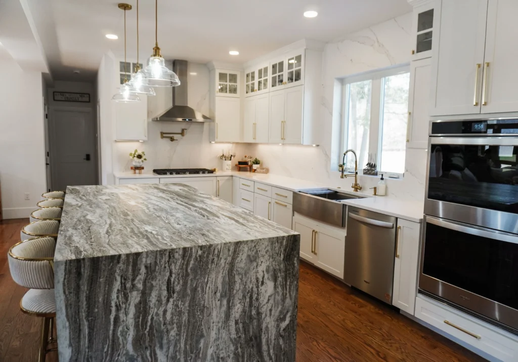 Modern kitchen featuring a large marble island, white cabinetry, and stainless steel appliances.